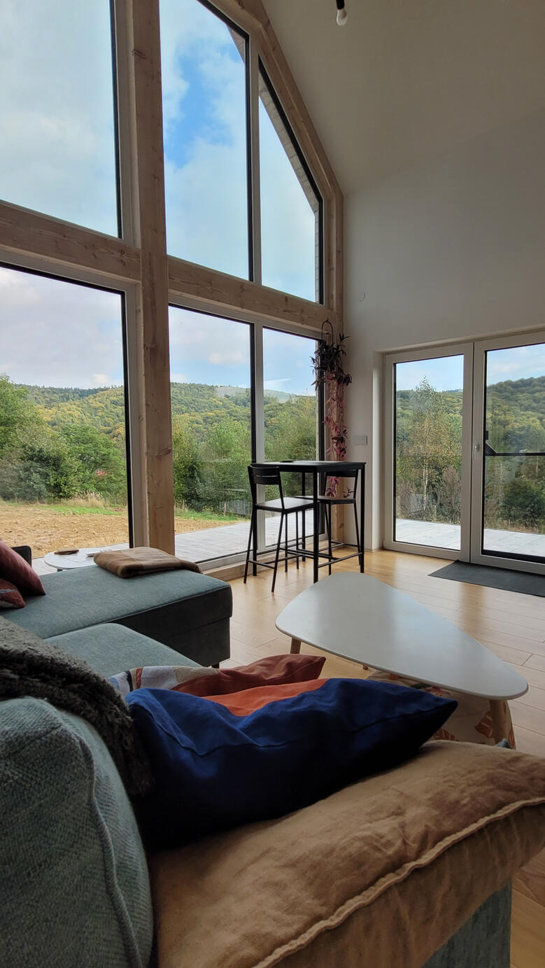 Panorama Pogórza Dynowskiego widziana z przytulnego salonu. Duże przeszklenia łączą wnętrze z naturą, tworząc idealne miejsce na posiłek dla dwojga.